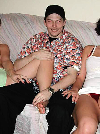 A naked chick with her coochie hanging out is sitting on a couch, while some fucking flower print shirt wearing dudes is taking pictures of 'em. 

```
Nude women on couch; dude in flowers checking camera
```