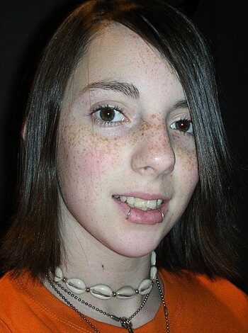 A busty broad in an orange tee grinnin' for da cam, 30 words
