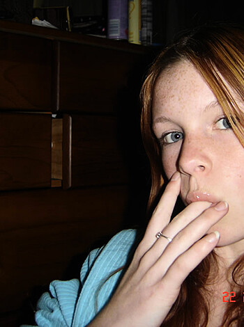 The girl blows smoke rings while holding a cancer stick between her lips.