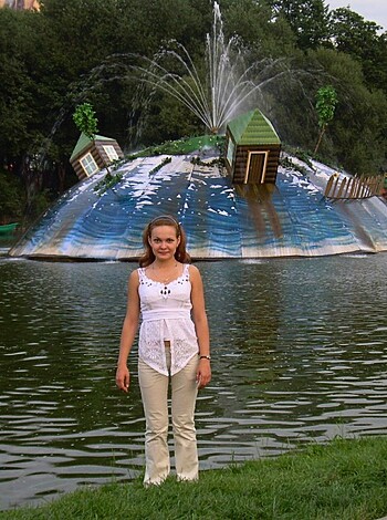 Here's a slutty teenager with her tits hanging out and ass showing, posing next to some stupid water spraying shit.