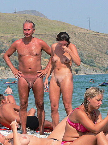 The image shows three people, two of whom are nude and engaging in sexual activity at a beach party while the other is fully dressed.