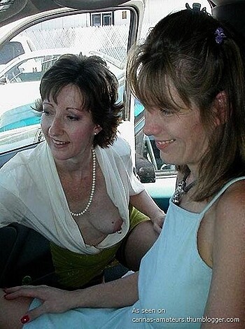 Two chicks are getting cozy in a ride, one's flashing her tits and grinning wide.