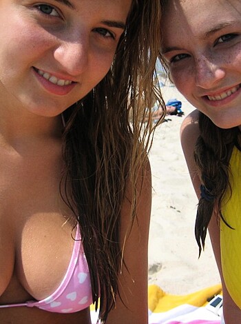 Two chicks in bikinis sunbathing on the sandy shore, flaunting their tits and ass.