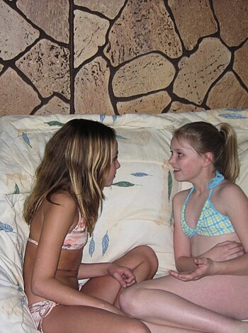 A couple of hotties in bikinis are chatting up a storm while sitting on a couch.