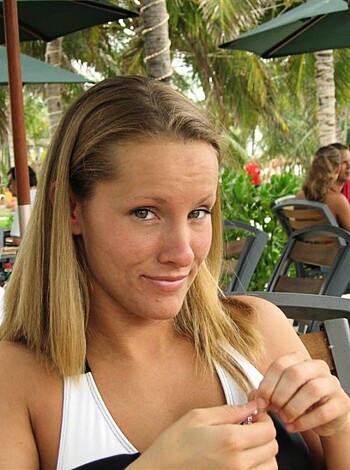 A hot bitch sits at a fucking table, sipping on some fucking drink while wearing a white tight-ass top.