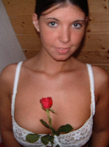 A smokin hot babe in a white bra with a luscious pair of boobs and a sweet ass, holding a giant fucking rose up in the air while she stares directly at the camera like a goddamn porno star.