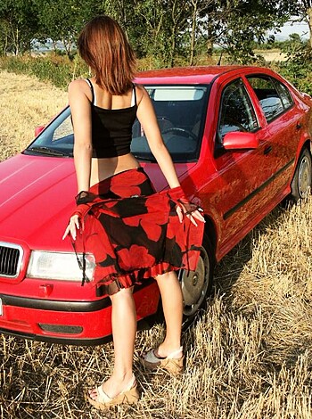 A hot babe flashing her tits while leaning against a shiny sports car.