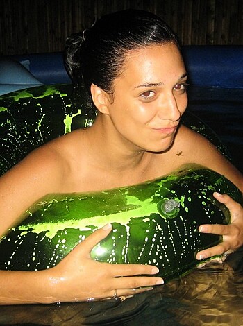 A nude babe chilling on a green turtle raft, floating in a swimming pool.