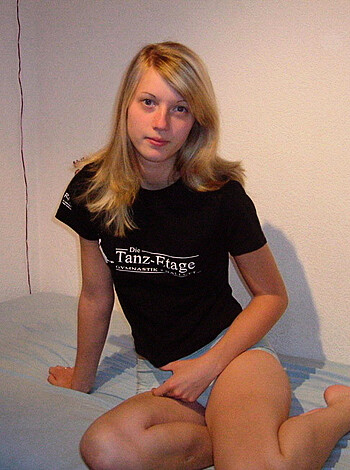 Here's a fucking photo of some hot bitch chillin' on her bed, with those tight jean shorts clinging to her thighs and that shit-eating grin on her face. She's wearing a black t-shirt and lookin' all fuckin' casual like she don't give a shit, but you know she wants some dick in the worst way.
