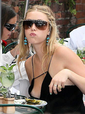 A busty, scantily-clad chick in a halter top is sitting at a table, shoving pizza in her mouth while flashing some serious cleavage, wearing tight earrings and shades. Her tongue's out, dude!