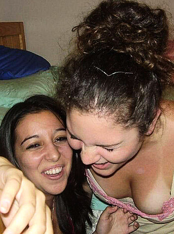 Here's the vulgar description of the image: The girl is going down on a chick while they snuggle in a bed, smiling their faces off.
