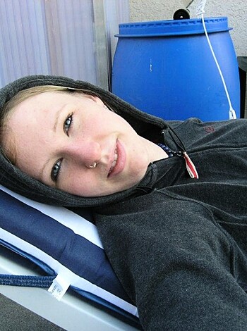 A young adult female is lying nude on her back with a hoodie draped over her body, staring directly into the camera lens.
