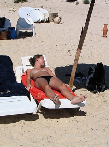 A chick with her cunt hanging out is getting some rays on the sand.