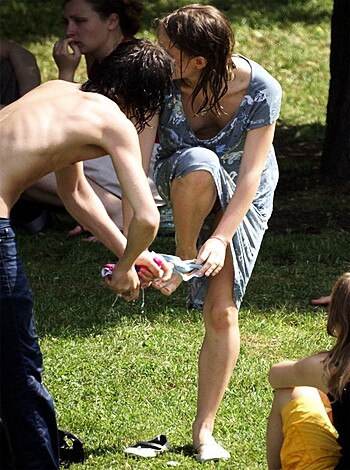 Here's the vulgar description: "In this image, you can see a d*ckhead moron helping some slutty b*tch wash her stinky foot while they both stand on some stupid grass. The whore is wearing a skanky dress and holding a water bottle in her other hand."