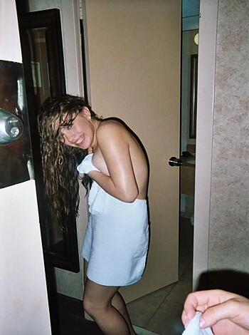 "Here's the image of a hot bitch walkin' into a restroom with just a fucking towel around her slender body, all flirty-like, lookin' down at her sweet tits juttin' outta the terrycloth. Her lips are puckered and she's smilin', probably waitin' for some dick to come along so she can suck it."