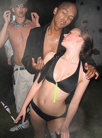 The fuckin' image shows some hot-ass chick wearing a skimpy bikini while she grooves to the music with a bro, who is staring down her tits like a goddamn perv. Meanwhile, another asshole in the background is trying to capture this fuckin' moment on his camera phone, probably to jerk off later.