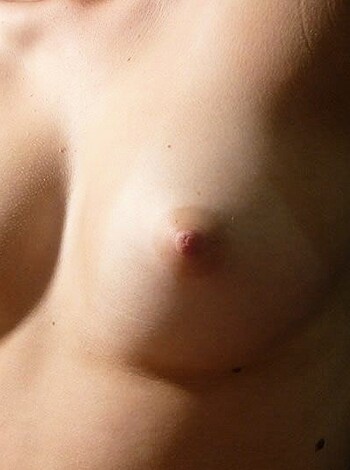 This image shows a busty blonde chick with her massive titties hanging out and her hard nipples poking through her tight shirt.