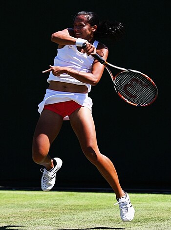 A busty blonde babe with boobs bouncing in a white tennis dress, pink kicks, and tight red shorts fucking around on the court.