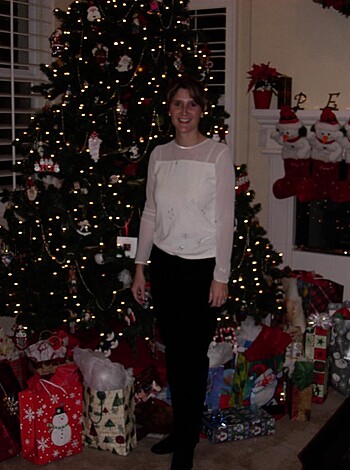 A bitch dressed in black panties and a tight white t-shirt is standing next to a Christmas tree filled with presents, while she flashes her dick and grins at you like a horny slut.