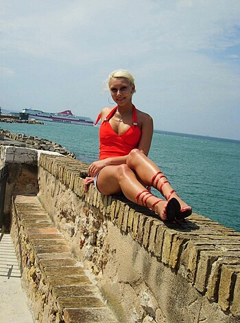 A hot chick wears sexy swimwear while posing on a brick wall, feet dangling over the ocean.