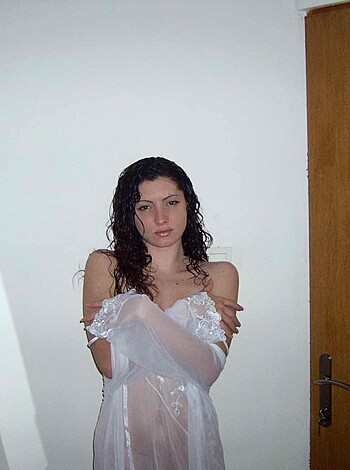 A completely nude babe is posing against a pristine white wall with her hands resting on her waist, revealing her juicy ass and massive tits.
