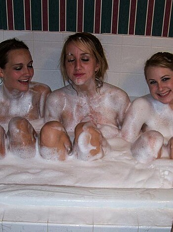 This photo features several topless women enjoying a bubble bath together, their ample breasts and wet hair slicked back as they giggle with each other.