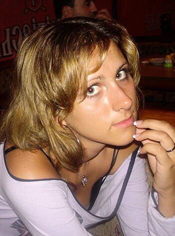 A hot blonde babe with a tight t-shirt and big boobs reaches up to touch her smooth cheek while giving the camera a sexy come hither look.