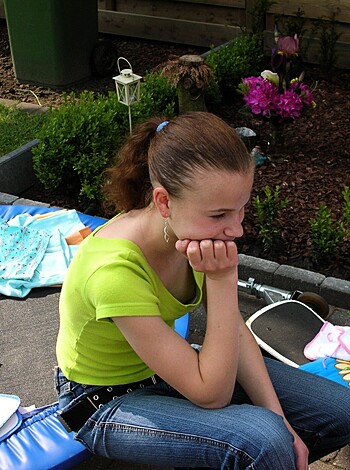 "Busty teen babe with big tits sucks on her fingers while she sits outside on her ass cheeks, smiling seductively."