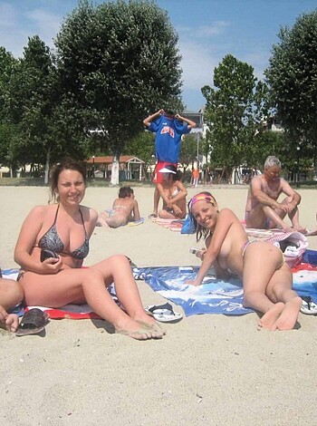 Beachgoers sunbathe topless, grinning like idiots amidst sandy tits 'n' asses.