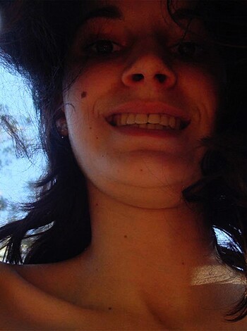 Image of a smiling busty titty bitch naked on her back with her arms above her head, showing off those perfect boobies while she grins like a fuckin' idiot.