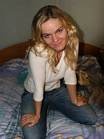 The chick in denim ass-huggers is slumped on the mattress, her arms crossed over her cleavage in an unflattering white t-shirt.