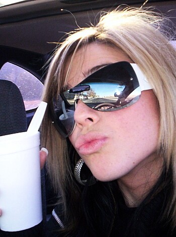 This bitch is sippin' her fucking coffee with those stupid shades on, like she's some kind of badass chick. But really, all she's doin' is trying to hide that ugly ass face from the rest of us normies who got better shit to do than stare at her ugly mug all damn day.