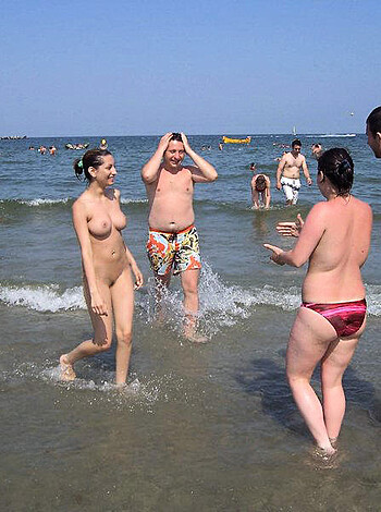 A chick in a string bikini scopes out some dong while lounging on the sandy shoreline with a nude dude.