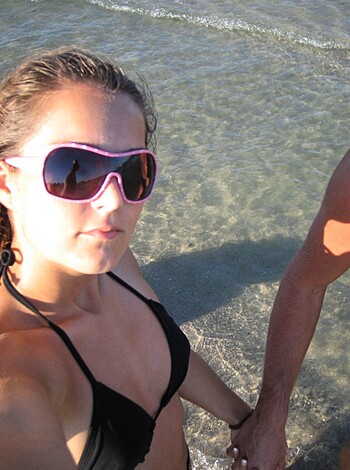 Vulgar Description: This is a picture of some hot chick in a bikini, standing on the fucking beach, holding hands with some dude while they take a selfie.