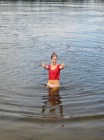 Here's the vulgar description of the image: A busty broad dick-diving in some water, giving two thumbs up and flipping the bird at the camera.