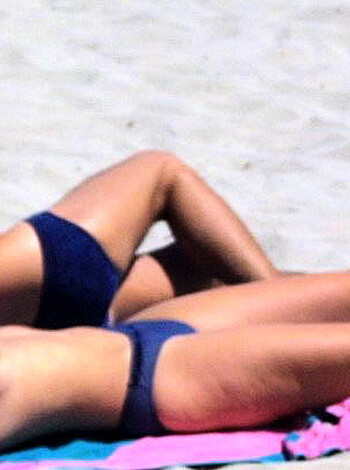 Three nude people laying on a sandy shore, covered in bikinis and board shorts.