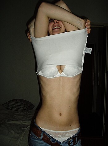 A nude chick is lying on her back, her tits hanging out of her white brassiere, with a pair of denim shorts on. She's fucking hot, man, but don't judge - it's her bedroom and she can do whatever the hell she wants in there.