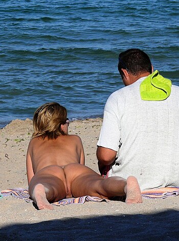 A shirtless dude is chillin' on the sand with some barely dressed babe while they both enjoy the scenery.