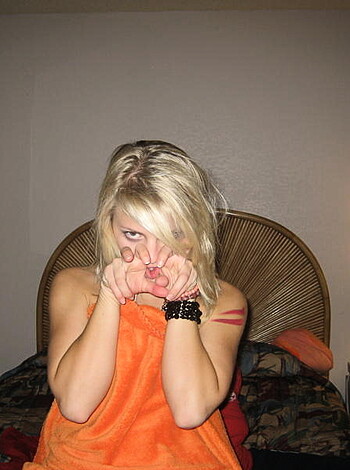 A naked chick posing like she just farted while sitting on her ass in her bedroom, looking all pissy and shit.