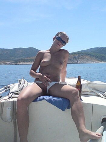 Here's a vulgar description of the image: "Fucking hot chick with tits out, drinkin' a fuckin' beer on a fuckin' boat, showin' off her pussy."