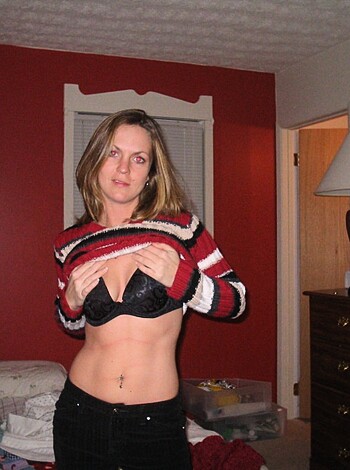 A slender brunette in her lingerie and an unflattering stripey sweatshirt poses for some selfies in a dank ass room.
