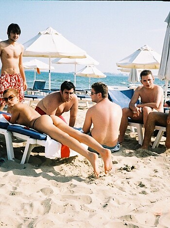 A bunch of dudes with no shirts on chillin' on the sandy shore, jawing away like a bunch of sea gulls.