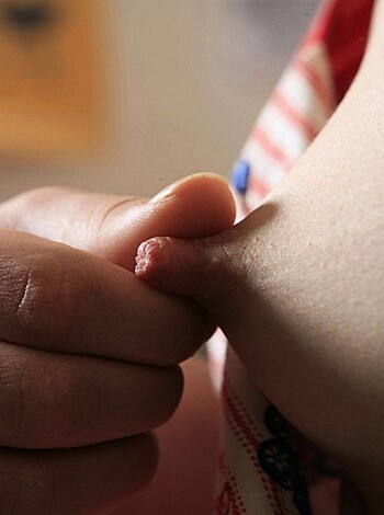 This image shows a small hand with tiny fingers lightly caressing a muscular thigh of a large man, creating a tender moment between the two individuals.