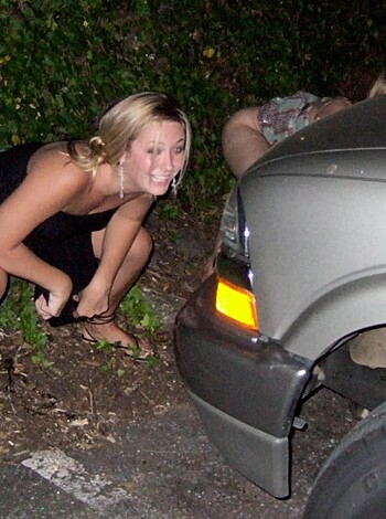 "Busty blonde chick with tits hanging out of her tank top grinning beside a car door while showing off her matching bling."