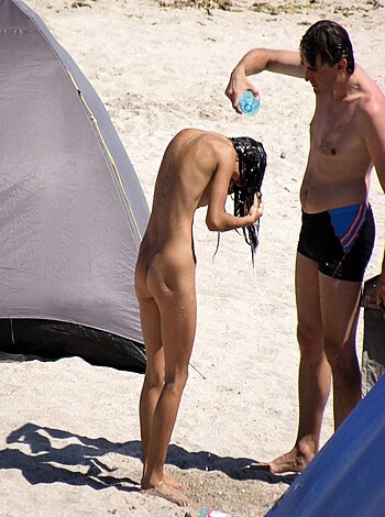 A naked bitch is getting douched down by some dude on the shore.