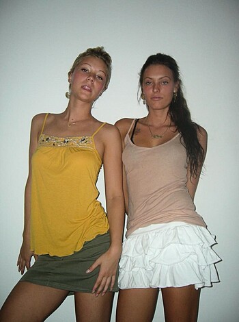 Here's the factual description of the image: A busty, curvy chick wearing a tight-ass yellow top that shows off her perky tits, and a sexy black miniskirt that hugs her round ass, posing for a photo with her arms akimbo and a cockteasing smile on her lips.