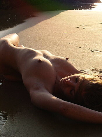 This fucking picture depicts a bare-assed bitch lying down on her back on wet shit at the shore during sundown, with most of her ass in the water.