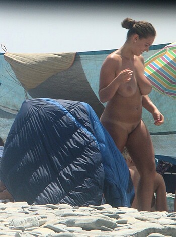 A chick struts bare assed down the sandy shore while surrounded by a bunch of dicks gazing at her.