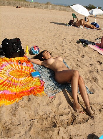 A naked bitch lounges on some sand with her tits out and her pussy hanging out, just chilling like a total fucking whore.