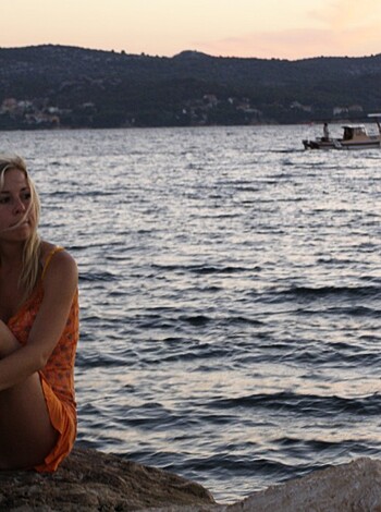A young slender chick in a short orange dress lights up a cancer stick while leaning on the harbor's edge with her legs spread open for all to see.